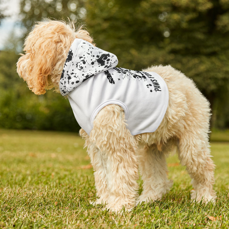 A fluffy Golden Doodle wearing a white shirt with the text 'Sailor Dogs - Paws for Adventure,' sitting on a sailboat deck with a serene ocean and mountain view in the background.