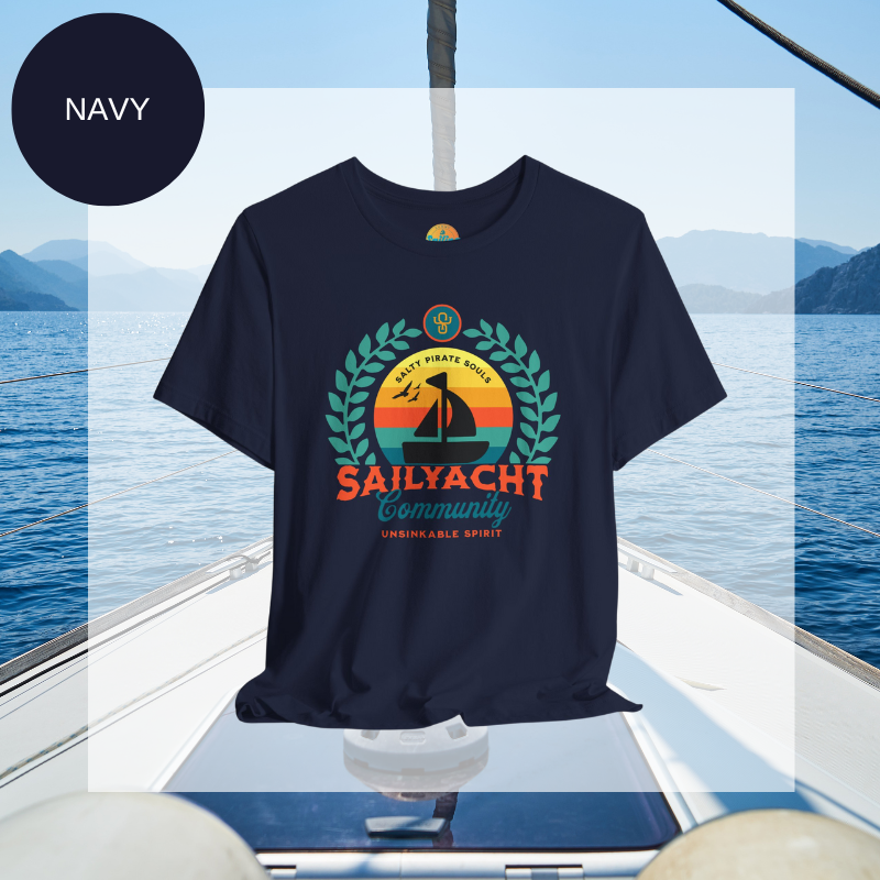 Navy blue unisex t-shirt featuring a vibrant 'Sailyacht Community' design with a sailboat, laurel wreath, and retro sunset, displayed on a yacht deck background.