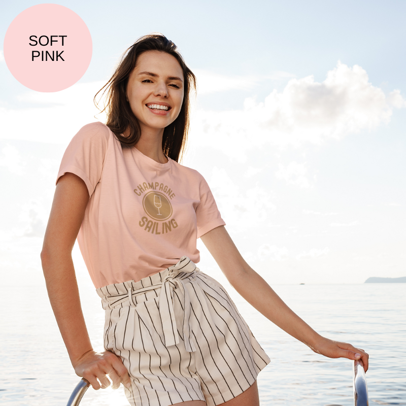 Soft pink t-shirt featuring a minimalist design with the text 'Champagne Sailing' in elegant gold lettering and a simple champagne glass icon, perfect for lovers of luxurious sailing vibes.