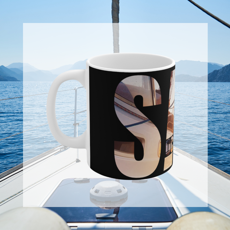 Black coffee mug with bold typography spelling 'SAIL OCEAN WIND,' featuring a vibrant image of a sailboat bathed in warm sunlight, perfect for sailing enthusiasts.
