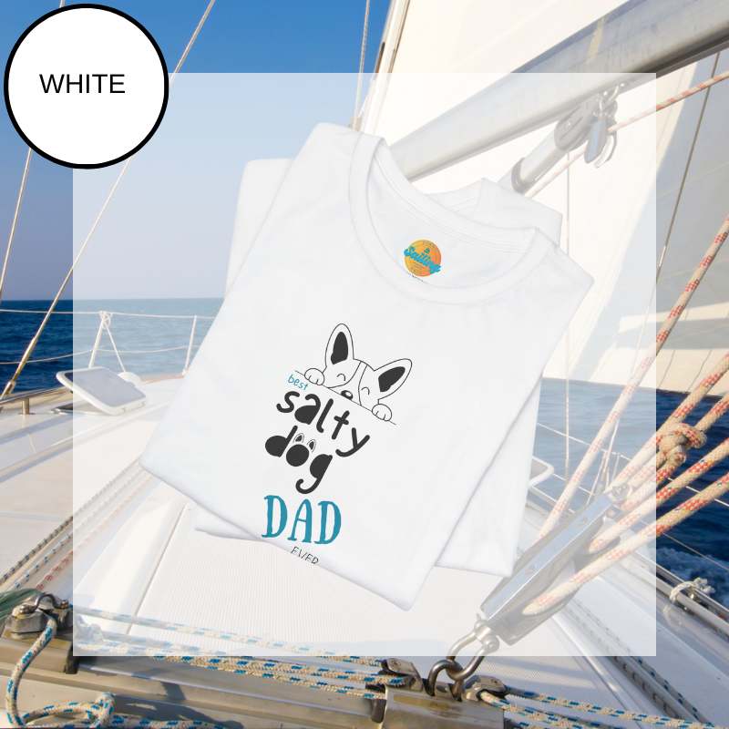 White t-shirt featuring the text 'Best Salty Dog Dad Ever' in playful fonts. The design includes an illustration of a cute dog's face peeking over the words, combining nautical and pet-loving themes. The background showcases a serene sailing scene with ropes and a yacht deck.