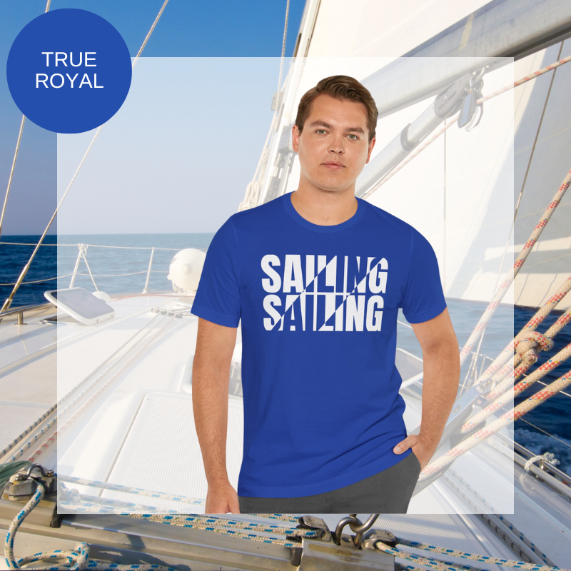 Royal blue unisex t-shirt with bold white text design reading 'Sailing Sailing,' displayed on a yacht deck with a nautical background.