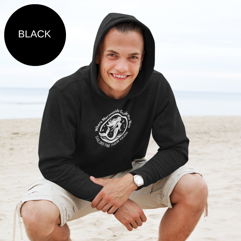 Black hoodie featuring a whimsical design of a mermaid with the text 'Where Mermaids Guide the Way, Sailors Find Their Haven,' ideal for ocean lovers and sailing enthusiasts.