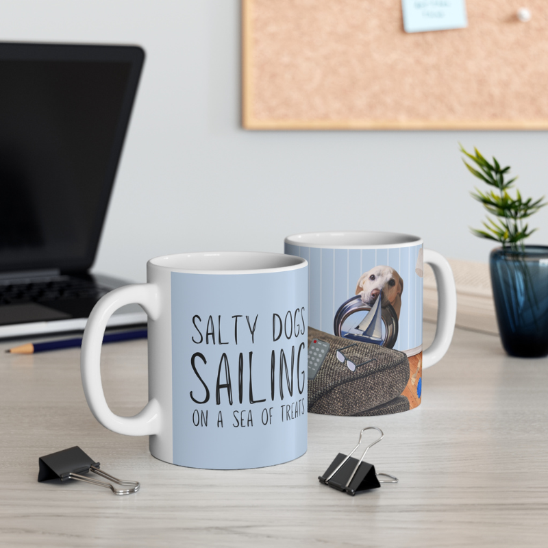 Light blue coffee mug featuring the text 'Salty Dogs Sailing on a Sea of Treats' with a playful illustration of a dog holding a food bowl with a sailboat in it, perfect for dog-loving sailors.