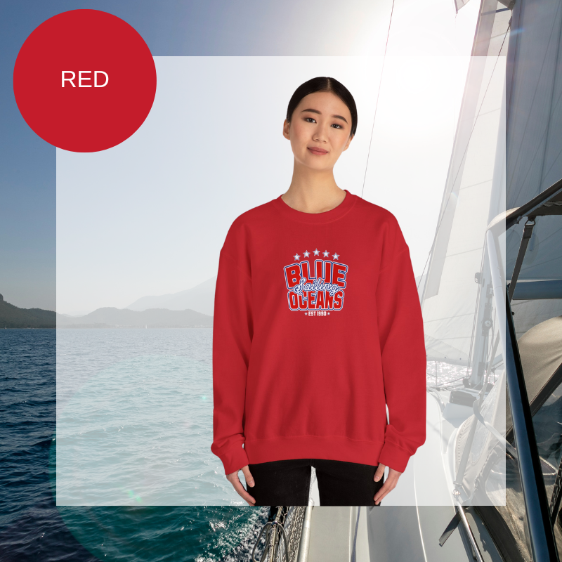 Red women's sweatshirt with a bold "Blue Oceans Sailing" print, featuring stars and a nautical-inspired design, displayed against a sailing-themed background.