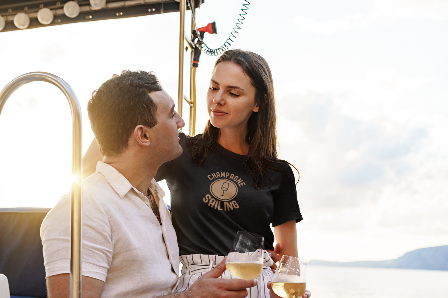 a couple sitting on a boat, drinking wine, woman is wearing a black t-shirt with print Champagne sailing