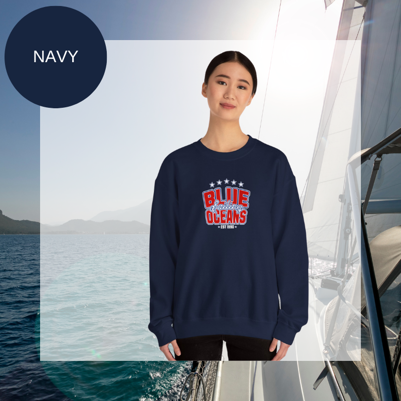 Navy women's sweatshirt with a bold "Blue Oceans Sailing" print, featuring stars and a nautical-inspired design, displayed against a sailing-themed background.