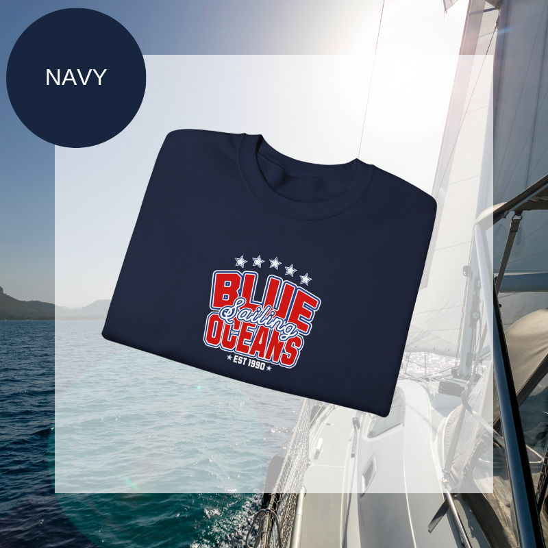 Navy women's sweatshirt with a bold "Blue Oceans Sailing" print, featuring stars and a nautical-inspired design, displayed against a sailing-themed background.