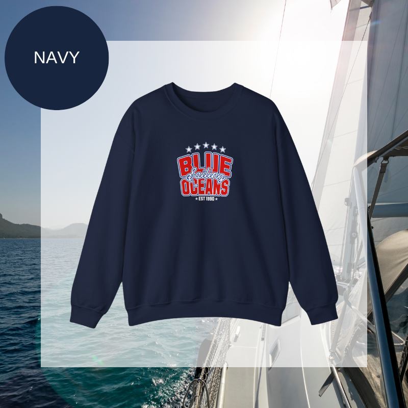 Navy women's sweatshirt with a bold "Blue Oceans Sailing" print, featuring stars and a nautical-inspired design, displayed against a sailing-themed background.