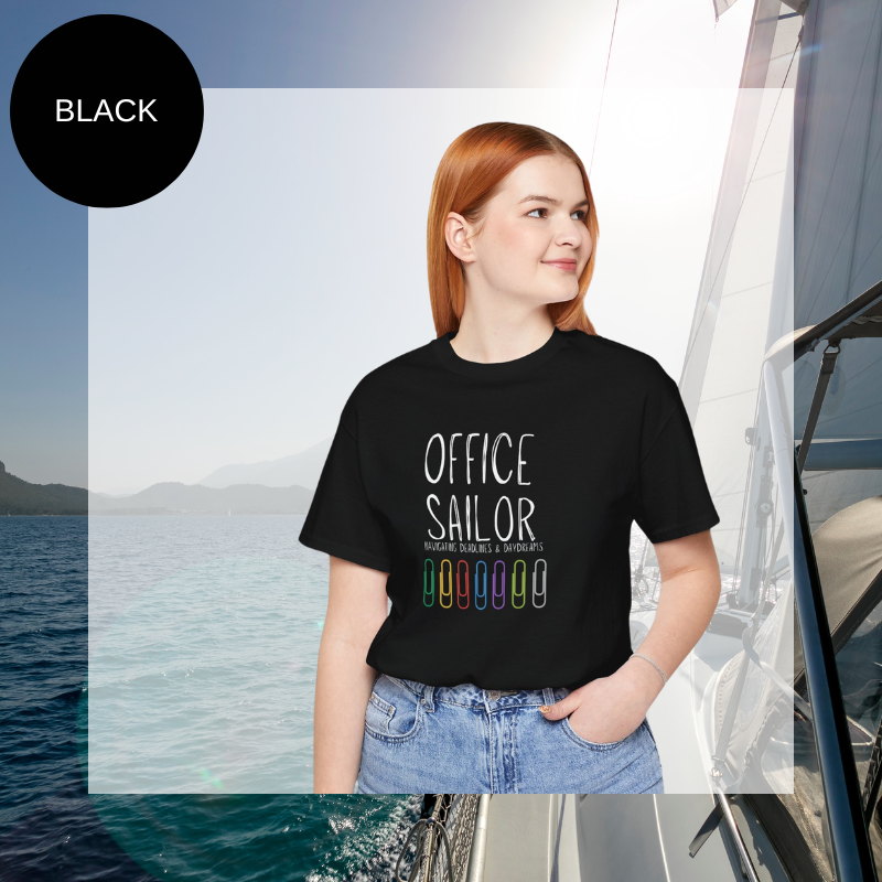 Black women's t-shirt with the text 'Office Sailor: Navigating Deadlines & Daydreams' and colorful paperclip illustrations, displayed on a sailing-themed background.