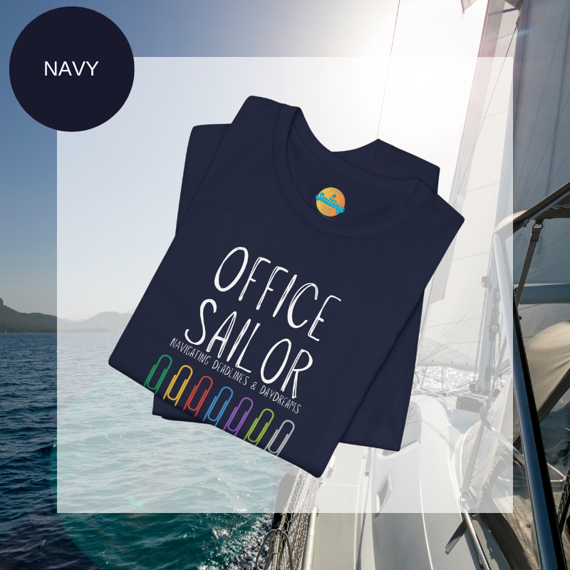 Navy women's t-shirt with the text 'Office Sailor: Navigating Deadlines & Daydreams' and colorful paperclip illustrations, displayed on a sailing-themed background.