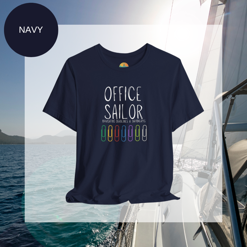 Navy women's t-shirt with the text 'Office Sailor: Navigating Deadlines & Daydreams' and colorful paperclip illustrations, displayed on a sailing-themed background.