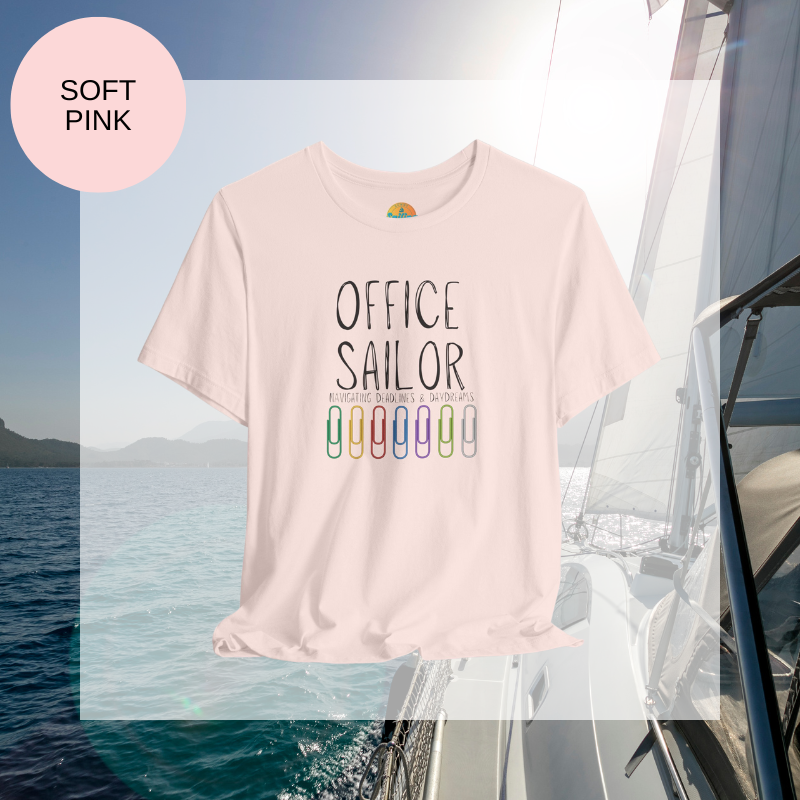 Pink women's t-shirt with the text 'Office Sailor: Navigating Deadlines & Daydreams' and colorful paperclip illustrations, displayed on a sailing-themed background.