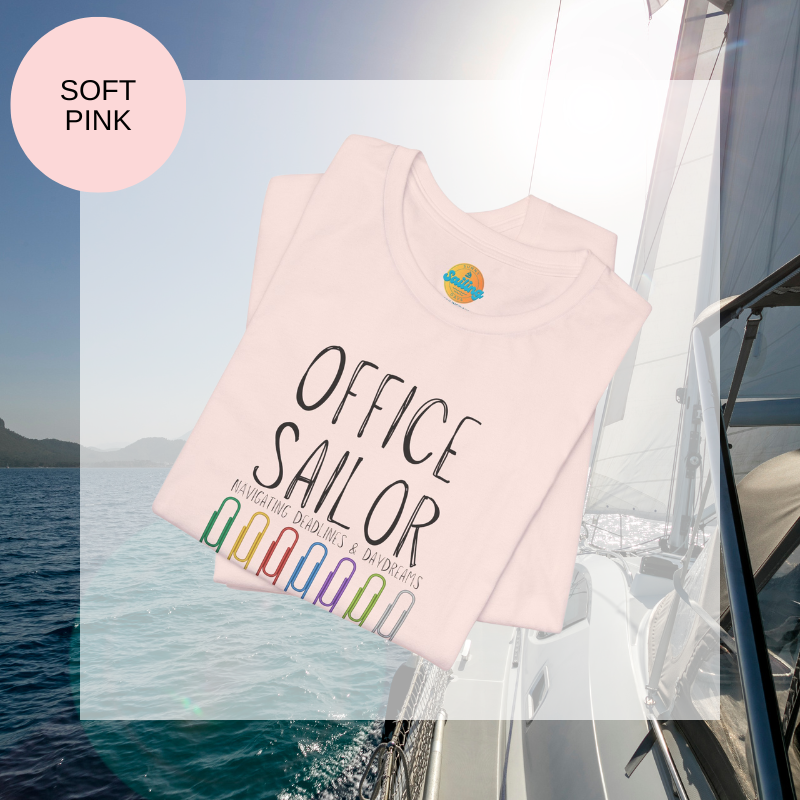 Pink women's t-shirt with the text 'Office Sailor: Navigating Deadlines & Daydreams' and colorful paperclip illustrations, displayed on a sailing-themed background.