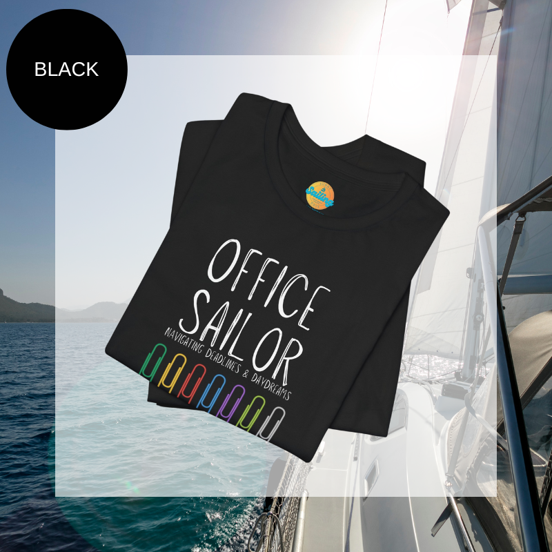 Black women's t-shirt with the text 'Office Sailor: Navigating Deadlines & Daydreams' and colorful paperclip illustrations, displayed on a sailing-themed background.