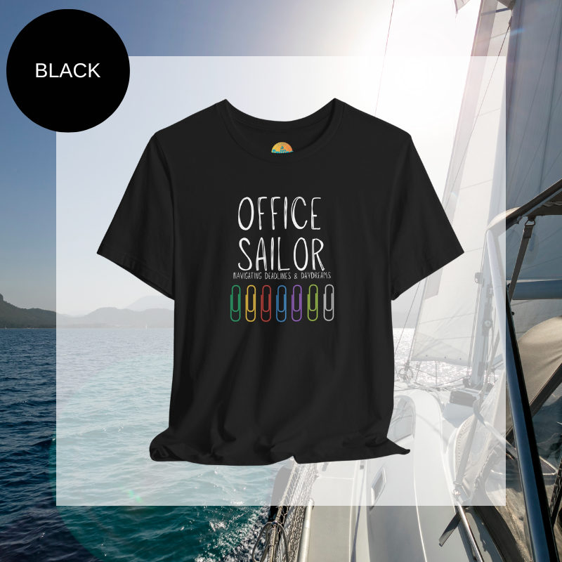 Black women's t-shirt with the text 'Office Sailor: Navigating Deadlines & Daydreams' and colorful paperclip illustrations, displayed on a sailing-themed background.